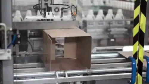 מכונה מרכיבה קופסת קרטון על מסוע אוטומטי בסביבת מפעל.